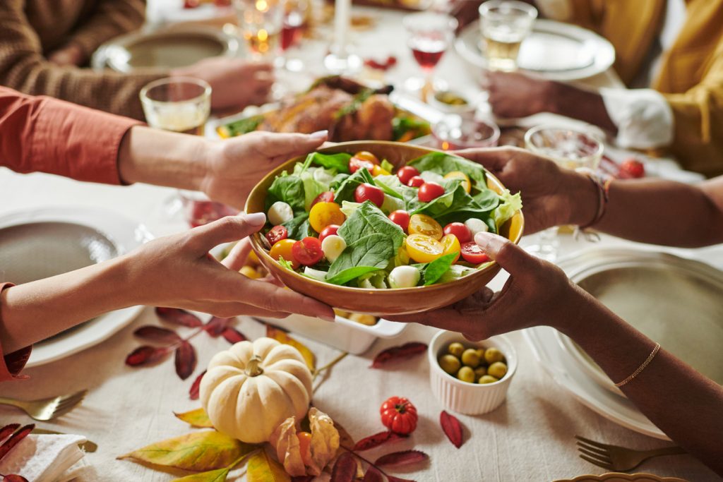 Hands sharing a fresh salad at a festive table, showing balanced holiday wellness tips.