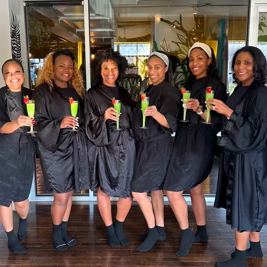 Group of Black women in robes smiling and holding green spa drinks at Iwi Fresh Garden Day Spa in Atlanta.