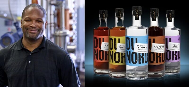 Chris Montana, founder of Du Nord Social Spirits, the first Black-owned distillery in the U.S., standing in a distillery alongside a selection of premium spirits from the brand."