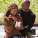 Black couple smiling as he gives her a gift, showcasing.