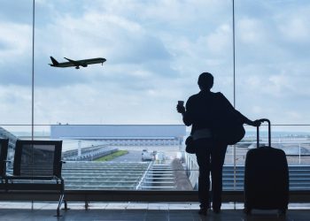 A woman in an airport lounge watches a plane take off, enjoying a moment of travel recovery and relaxation before her journey.