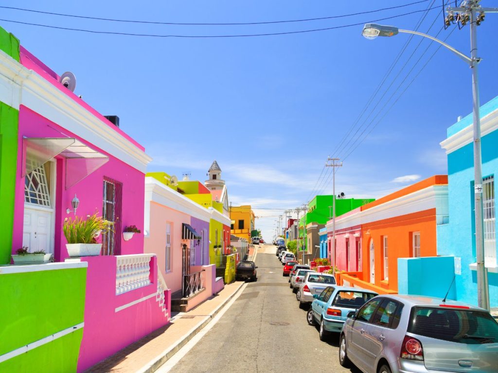 Colorful houses in Bo-Kaap neighborhood of Cape Town featuring bright pink, green, blue, yellow, and orange buildings lining a narrow street with parked cars