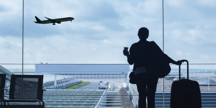 A woman in an airport lounge watches a plane take off, enjoying a moment of travel recovery and relaxation before her journey.