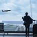 A woman in an airport lounge watches a plane take off, enjoying a moment of travel recovery and relaxation before her journey.