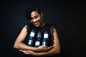 Woman with curly hair smiling while holding three candles against a dark background.