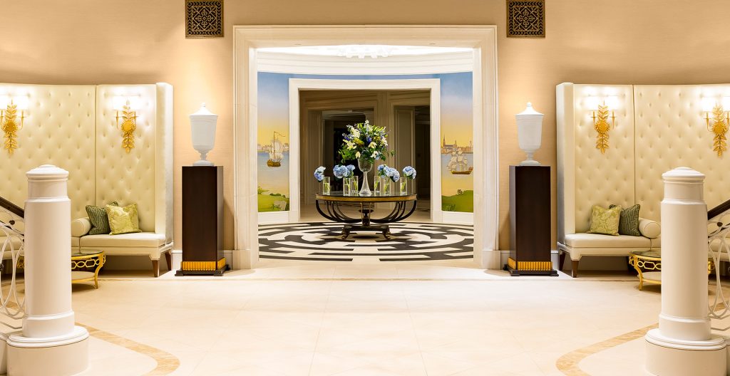 Beautiful hotel lobby with cream walls, cushioned seating, and flowers on a round table.