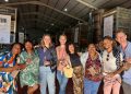 Wine festival lovers holding glasses and smiling together at an indoor tasting event with wine tanks and banners visible.