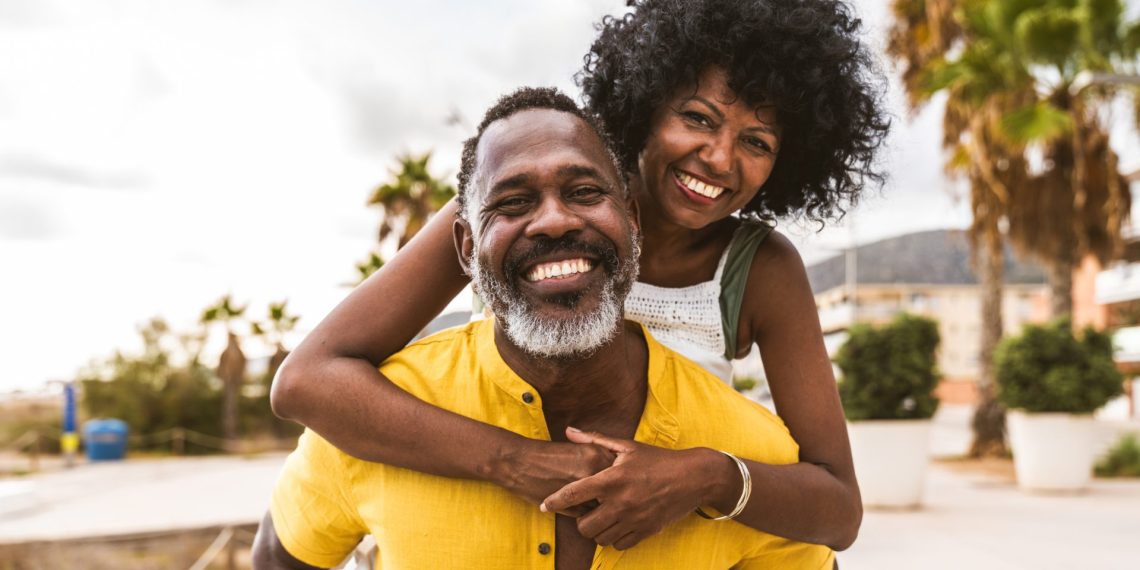 Happy Black couple over 40 embracing and smiling in a tropical destination with palm trees, representing mature Black travelers enjoying luxury vacation experiences.