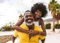 Happy Black couple over 40 embracing and smiling in a tropical destination with palm trees, representing mature Black travelers enjoying luxury vacation experiences.