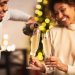 A smiling Black couple pours and shares glasses of sparkling wine during a festive celebration.