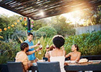 Friends sharing wine outdoors under a pergola, enjoying a relaxed garden meal. | wine travel guide 2025