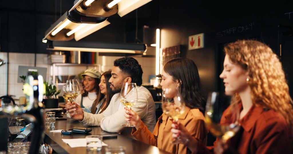 A diverse group of young adults enjoys a wine tasting at a modern bar.